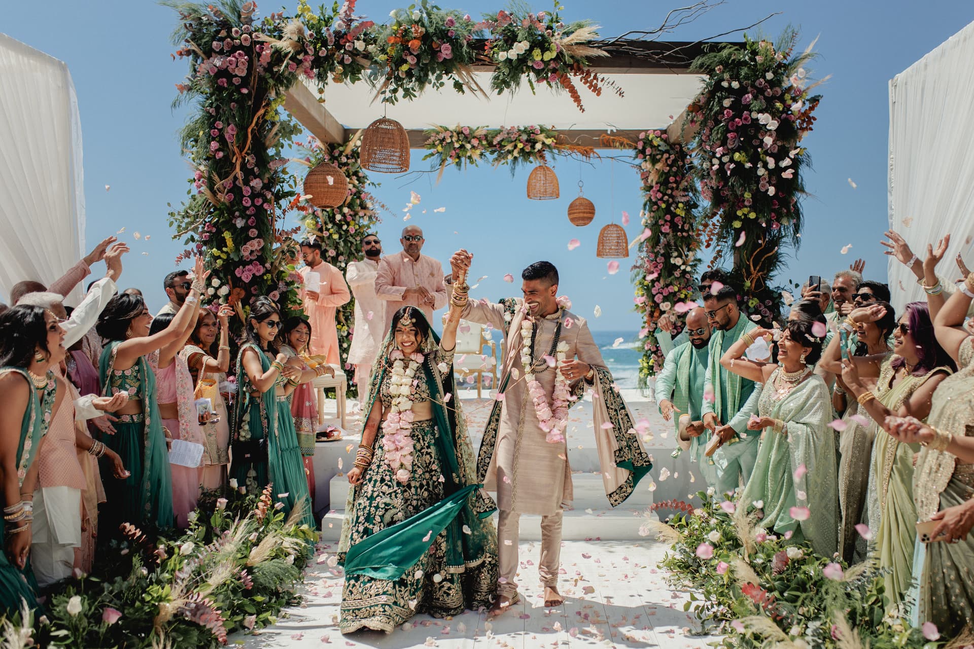 Newlywed couple celebrating beneath a floral structure by the sea