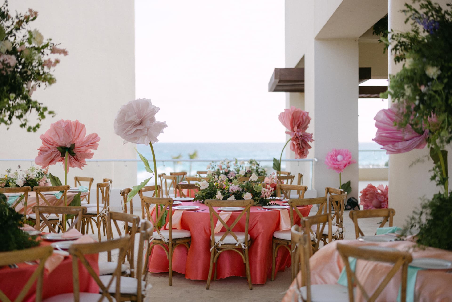Oceanfront reception tables framed by sculptural pink flowers