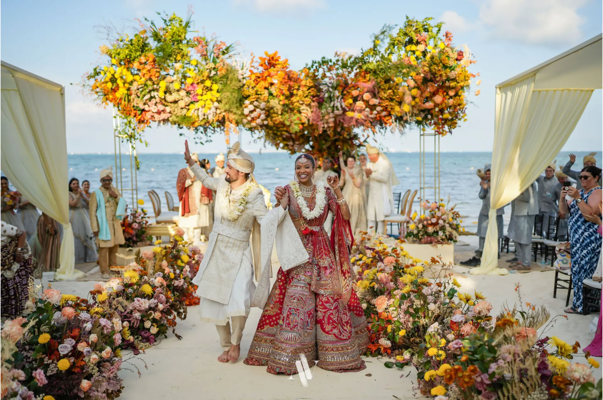 Newlyweds walking through a colorful seaside ceremony in the Riviera Maya
